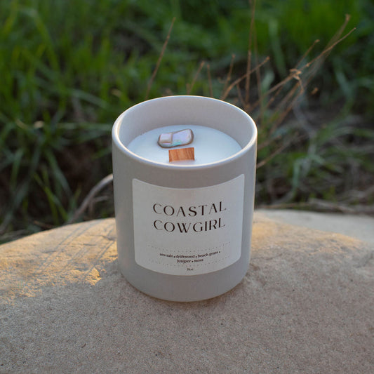 Candle labeled 'Coastal Cowgirl' on a rock with grass in the background