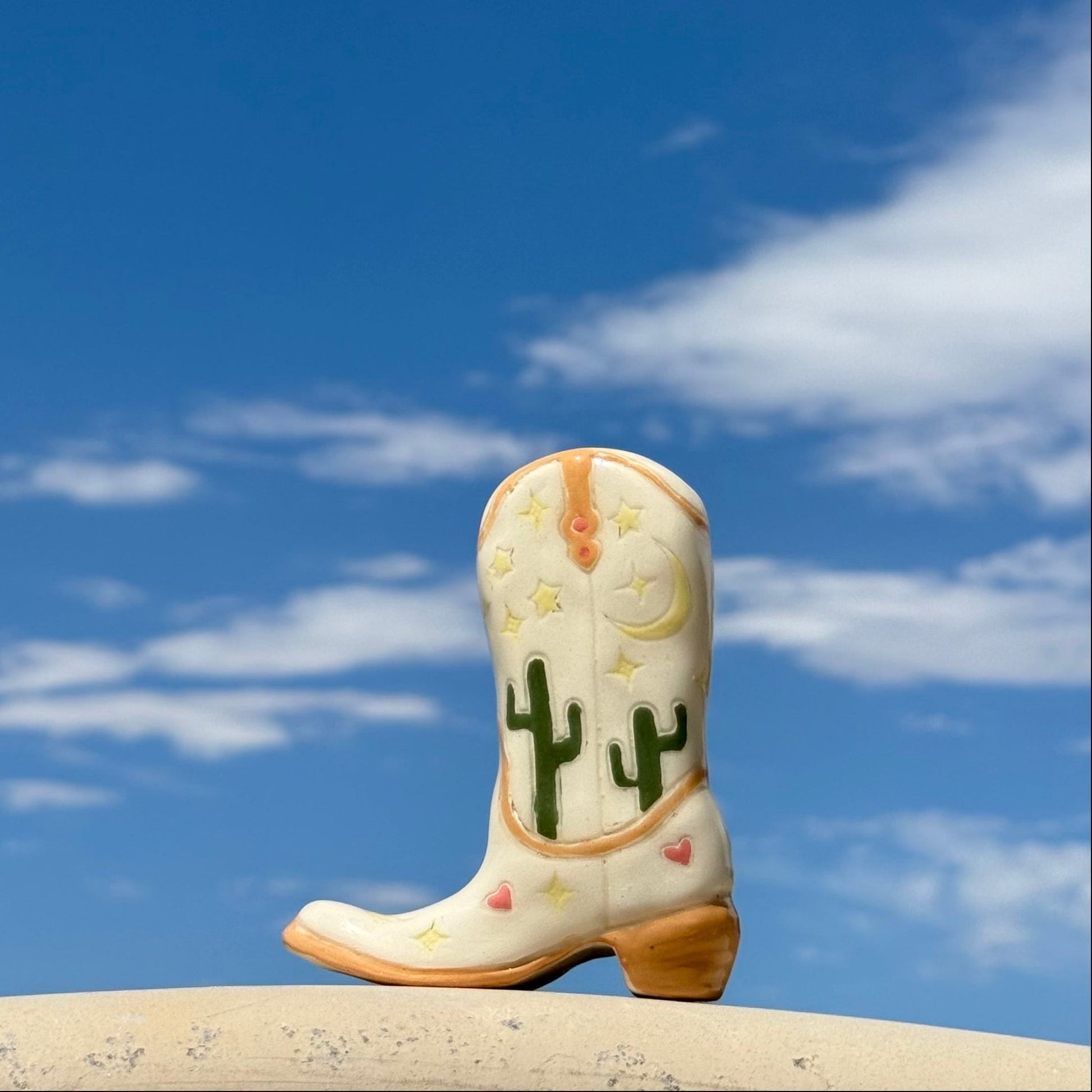 Cowboy boot with cactus design against a blue sky