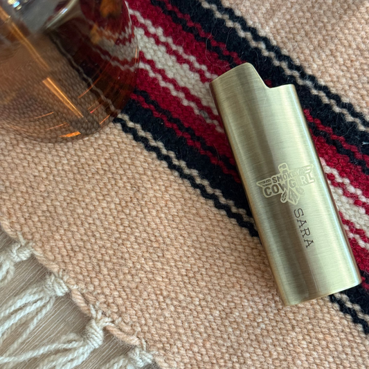 Brass lighter with 'Sara' branding on a patterned fabric background