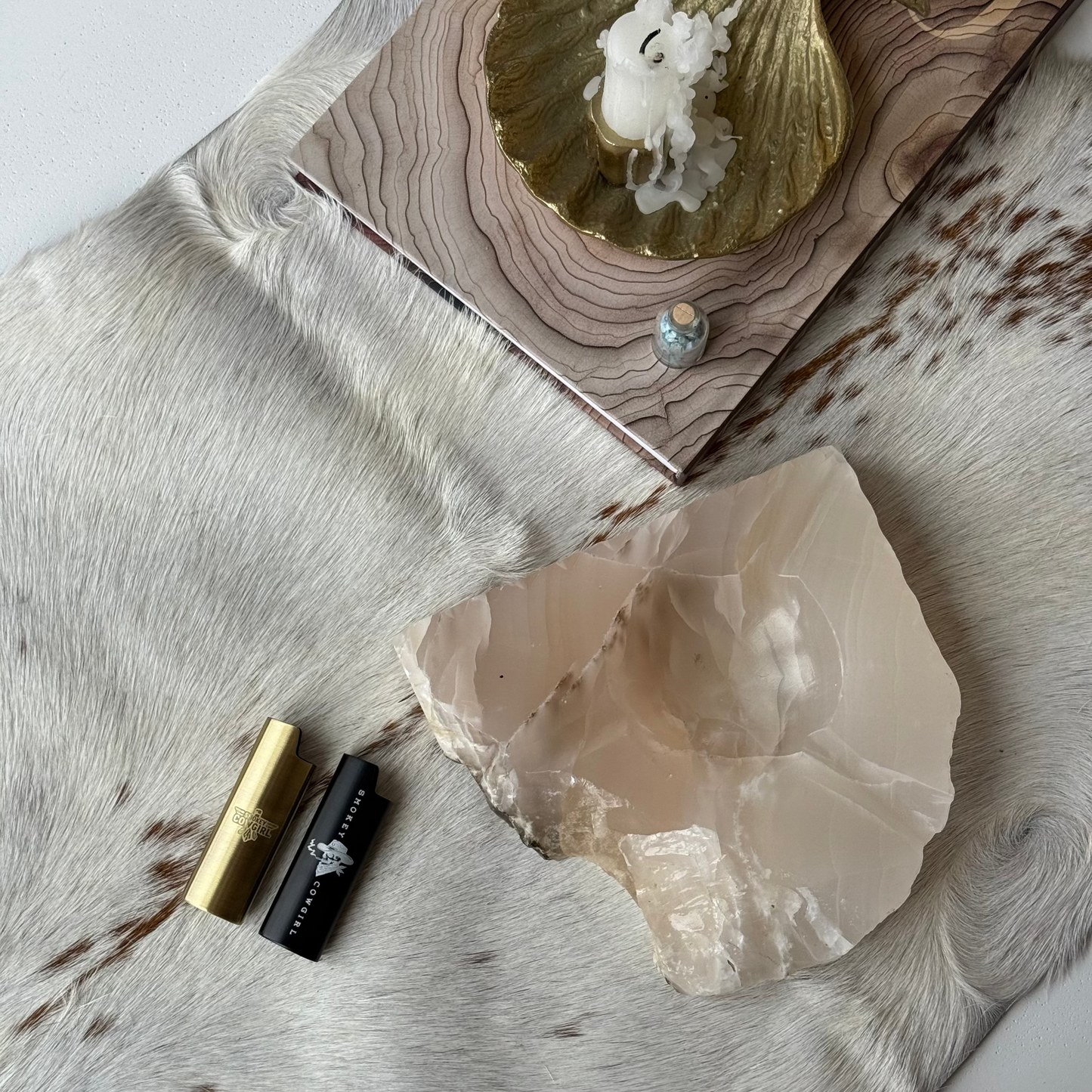 Decorative setting with a crystal, gold leaf, and candle on a textured surface.